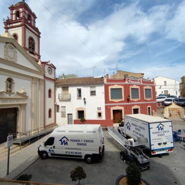 Fotografía de una calle con camiones de transporte y una plataforma elevadora para la mudanza